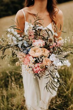 a woman standing in a field holding a bouquet of wildflowers and greenery