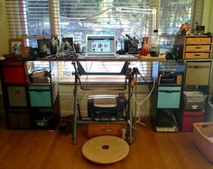 a computer desk sitting in front of a window with lots of clutter on it