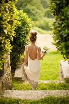 a woman is walking down some steps with flowers in her hand and wearing a white dress