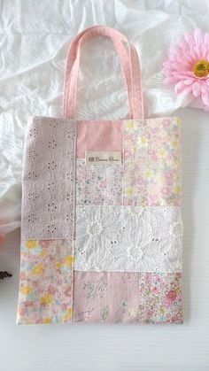 a pink and white tote bag sitting on top of a bed next to a flower