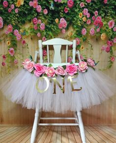 a white chair with pink flowers on it and the word one spelled out in gold