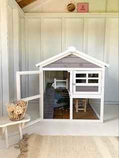 a small dog house made out of wood and white painted walls, with the door open