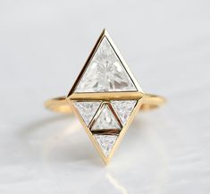 a gold ring with two triangular shaped diamonds on the front and side, sitting on a white surface