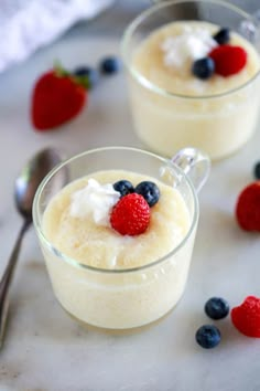 two glasses filled with pudding and berries on top of a white counter next to spoons