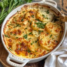 a casserole dish with potatoes and parsley in it on a wooden cutting board