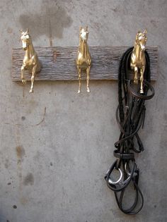 three gold horse heads are attached to a wooden hook with black cords and hooks on the wall