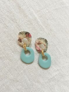 two pairs of blue and gold earrings on a white surface with floral print fabric in the background