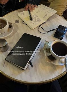 a person sitting at a table with two cups of coffee and notebooks on it