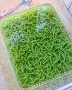 green noodles are in a plastic container on the table, ready to be put into an oven