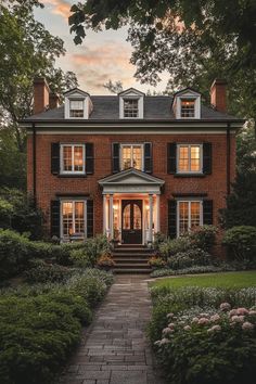 a large red brick house with lots of windows and plants in the front yard at dusk