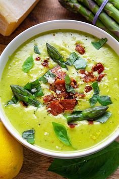 a white bowl filled with broccoli soup next to asparagus