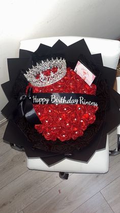 a black and red birthday cake with a tiara on it's head sitting on a white chair