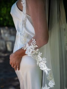 the bride is holding her dress while she wears an arm piece with white flowers on it