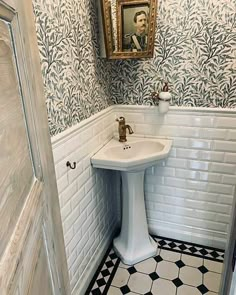 a white pedestal sink sitting in a bathroom next to a painting on the wall above it