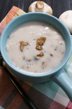 a blue bowl filled with soup next to mushrooms and spoons on a checkered table cloth