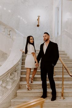 a man and woman are standing on the stairs in front of some marble staircases