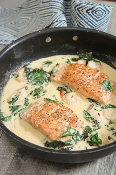 two salmon fillets are in a skillet with spinach and cheese on the side