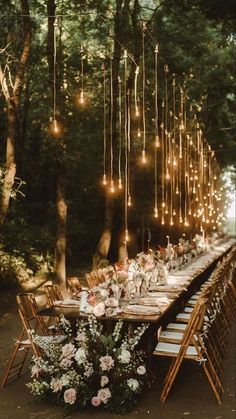 an outdoor dinner table with lights strung from the trees and flowers on it, surrounded by greenery