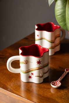 two coffee mugs sitting on top of a wooden table next to a potted plant