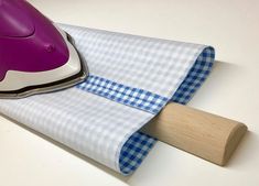 a purple and white steam iron sitting on top of a blue checkered cloth next to a wooden paddle