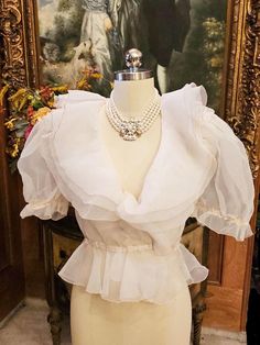 Original Price 145.00 A beautiful vintage off white sheer organza evening blouse adorned with 3-tier ruffled large collars and puff sleeves. There are 3 tiers of organza layers on the beautiful collar which is edged with a thin line of ecru trim. The flounce, sleeves and waist also has the trim. The sleeves are gorgeous as they are large and puffy. The blouse had a hook and eye in front but the hook part needs to be replaced as it has been twisted and not workable. (Easy fix) (Last photo).  The eye part is on the blouse  is fine.  The elastic needs to be replaced in the sleeves and the waist and the cleaners can easily do that or the next owner can.  Both of these are easy fixes. Perfect with an evening skirt, slacks or jeans for this summer.  You just do not see blouses as pretty or elega 70s Blouse, White Ruffle Blouse, Evening Blouses, Evening Skirts, Ruffled Collar, Blouse Vintage, Character Outfits, Sheer Blouse, Favorite Things Gift