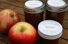 three jars of apple jam sitting on top of a wooden table next to two apples