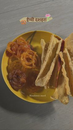 a yellow plate topped with a sandwich and some onion rings next to chips on a table