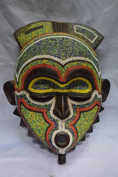 an african mask with multicolored designs on it's face and nose, against a white background