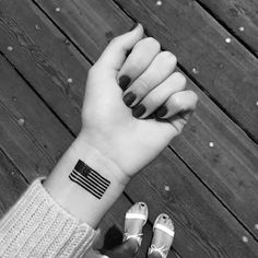 a woman's hand with a small american flag tattoo on her left wrist and the other arm