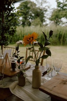 This shows a close up of a wedding dining table. The focus being on two cream coloured stoneware bottles with sunflowers. The vases are displayed atop a white muslin runner and surrounded by table rises and glassware. Farm Photos, Farm Photo