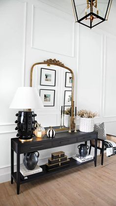 a black and gold console table with pictures on the wall behind it in a white room