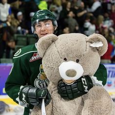 a hockey player holding a large teddy bear in his arms and wearing a green uniform