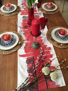 the table is set with red and white plates, vases, candles and flowers