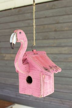 a pink birdhouse hanging from a rope with a flamingo on it's head