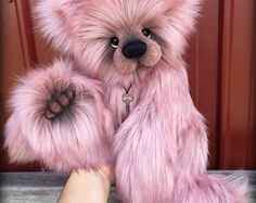 a pink teddy bear sitting on top of a wooden table next to a person's hand