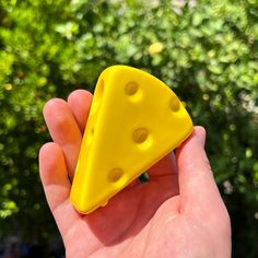 a hand holding a small yellow object with holes in it's middle and a green bush behind it