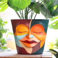 a potted plant with a face painted on the side and leaves in the background