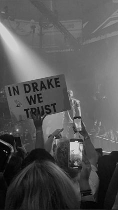 someone holding up a sign that says in drake we trust on it while people take pictures with their cell phones