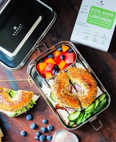 two lunch boxes with sandwiches, fruit and vegetables in them on a table next to an eco - safe lunchbox