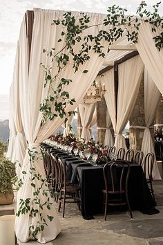 an instagram page with a table and chairs covered in white draping, surrounded by greenery