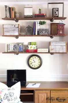 a desk with a clock and several shelves on it's wall above the computer