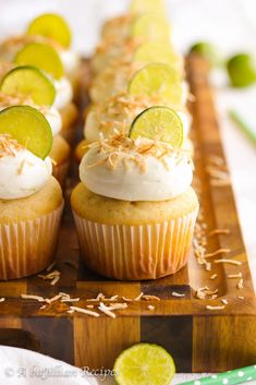 several cupcakes with lime slices and white frosting on a wooden tray next to some sliced limes