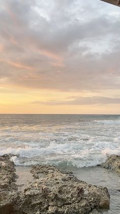 a person sitting on top of a rock next to the ocean under a cloudy sky