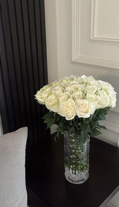 a vase filled with white roses sitting on top of a table next to a pillow