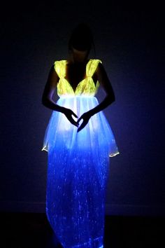 a woman standing in the dark with her hands on her hips wearing a blue and yellow dress