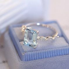 a ring with an aquamarinee stone sits on top of a blue velvet box