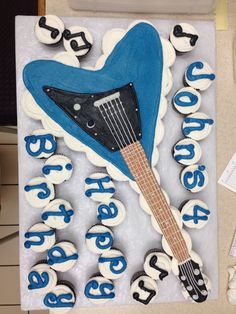 a blue and white cake with a guitar on it's side, surrounded by cupcakes