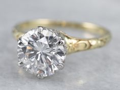 an old - fashioned engagement ring with a round brilliant diamond in the center, on a white surface