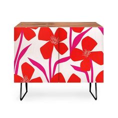 a red and white cabinet with flowers painted on the front, black legs and wooden top