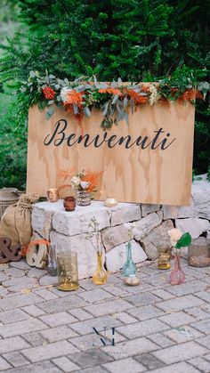 a wooden sign sitting on top of a brick floor next to flowers and candles in vases